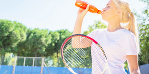 A tennis player drinks a sports drink